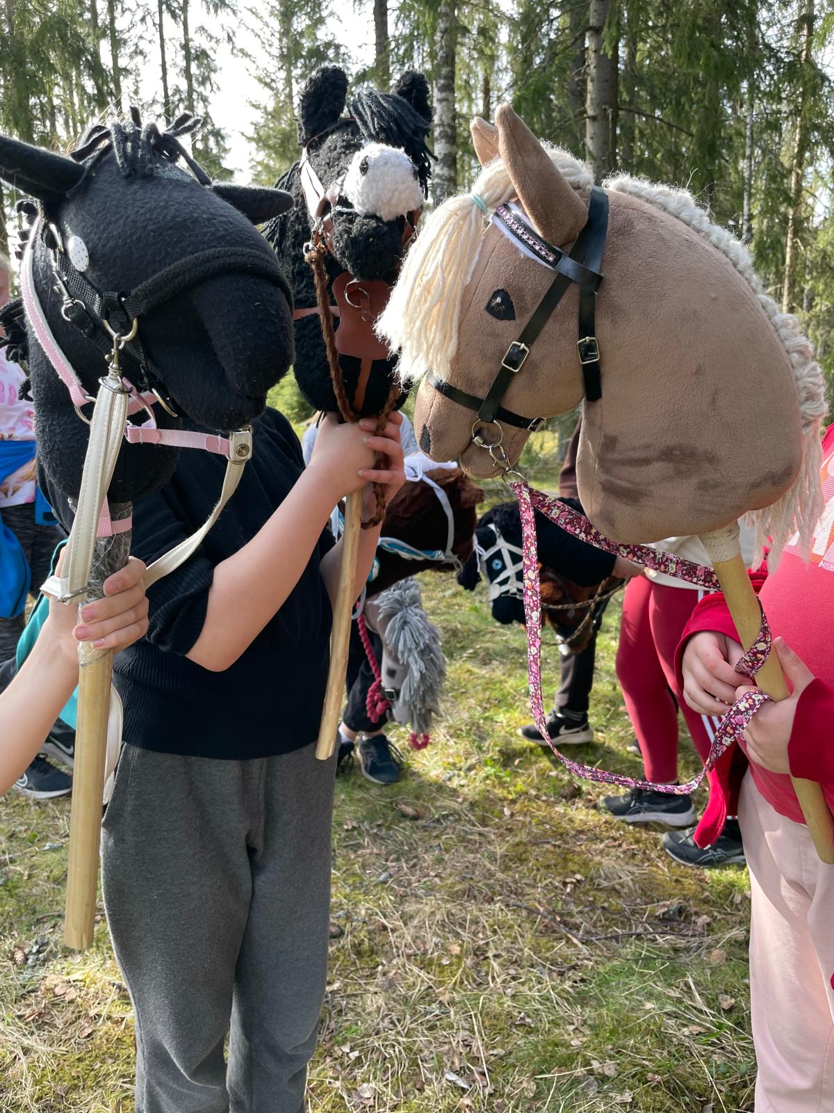Erivärisiä keppihevosia metsässä.
